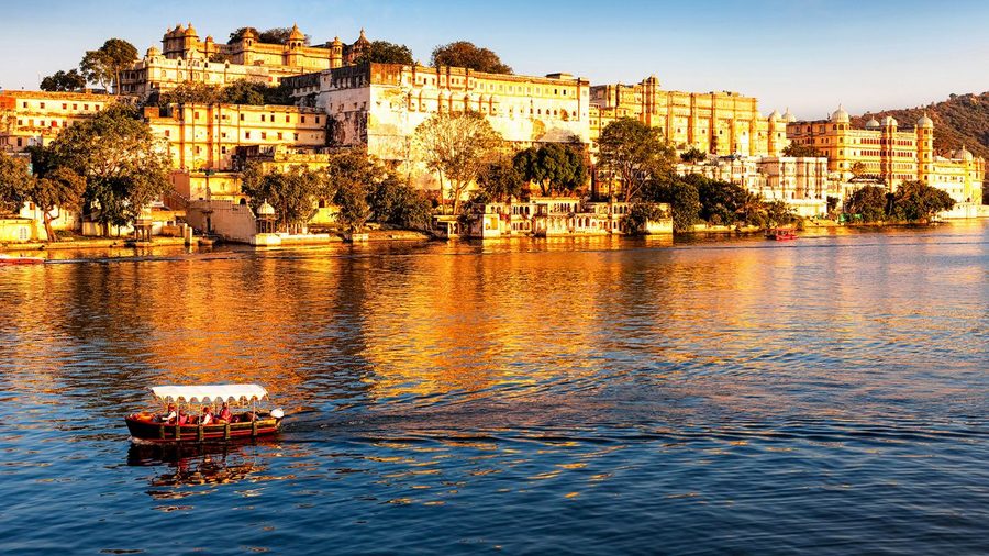 Golden hour view of Lake Pichola with the City Palace of Udaipur, Rajasthan, and a traditional boat on the water